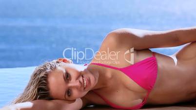 Smiling woman lying on side next to a swimming pool