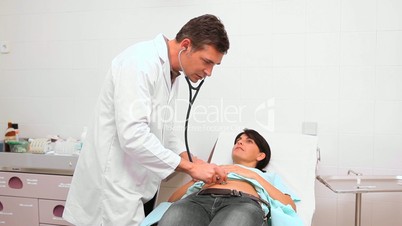 Serious doctor auscultating the belly of a patient