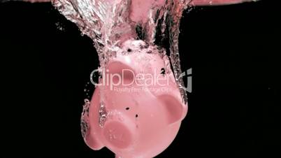 Pink piggy-bank diving in super slow motion into liquid