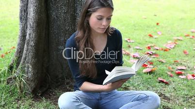 Woman reading a book next to a tree