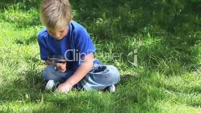 Boy looking at grass with a magnifying glass