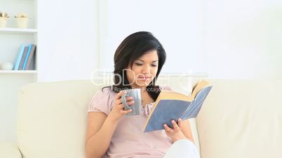 Asian woman reading a book while holding a mug