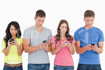 Four people standing beside each other and texting on their phon