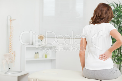 Woman sitting on a table while touching her back