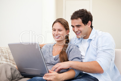 Couple sitting on a sofa while holding a laptop