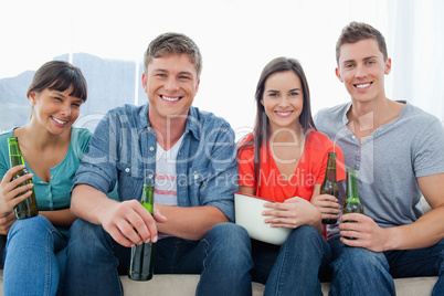 A smiling group sitting on the couch while holding beers