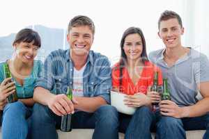 A smiling group sitting on the couch while holding beers