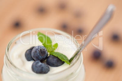 Close up of a pot of yoghurt with four leaves and blueberries
