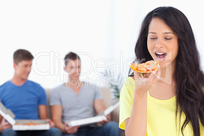 Woman about to eat a pizza slice as her friends sit behind her