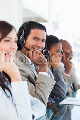 Young smiling call centre worker working among his business team