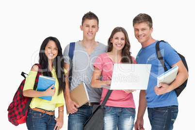 A smiling group of students holding a laptop while looking at th