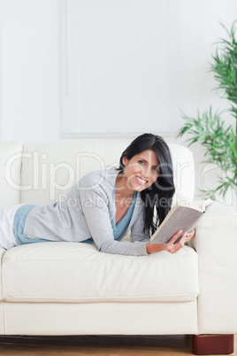 Smiling woman relaxing on a sofa while holding a book