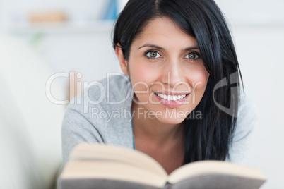 Woman smiling while holding a book in a couch