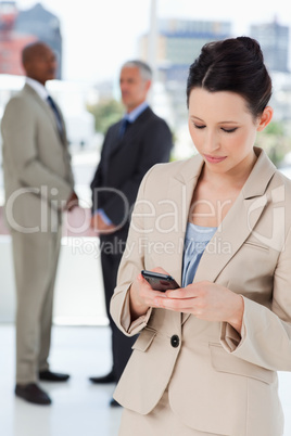 Serious businesswoman sending a text and executives behind her