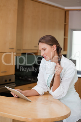 Woman holding a cup while looking at a tablet computer