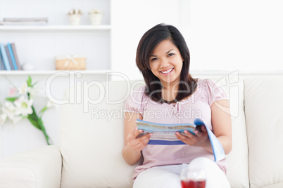 Woman sitting on a sofa while holding a magazine