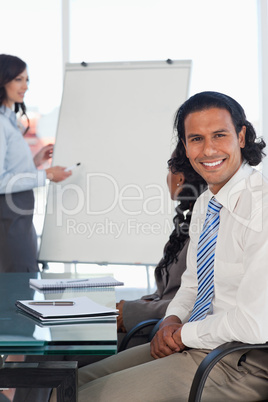 Smiling businessman sitting at a desk while listening to a prese