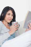 Woman reading a book while holding a grey mug