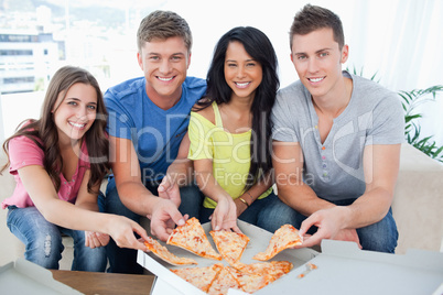 A group of friends taking a slice of pizza each as they look at