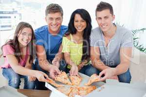A group of friends taking a slice of pizza each as they look at