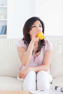 Woman sitting on a couch while drinking a glass of orange juice