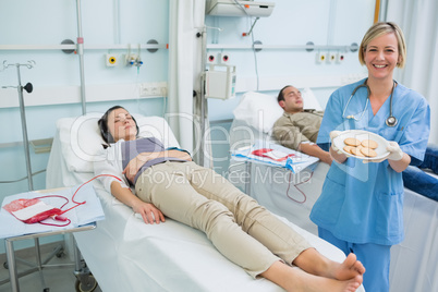 Nurse holding a plate of biscuits next to transfused patients