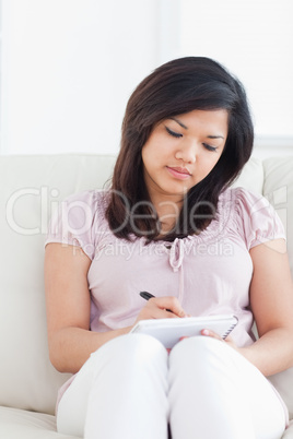 Woman sitting on a couch while writing on a notebook