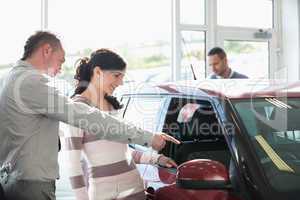 Car dealer pointing the interior of a car with a woman