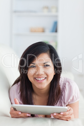 Smiling woman lying on a sofa while holding a tablet