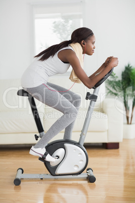 Side view of a concentrated black woman doing exercise bike