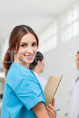 Nurse smiling while holding files and standing with a doctor and