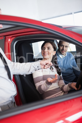 Smiling woman receiving keys from a salesman while sitting