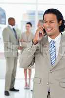 Businessman using a cell phone while his team is talking behind