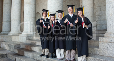 Five happy graduates posing the thumb-up