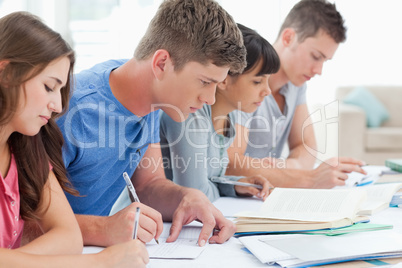 Side view of four students studying and writing together