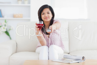 Woman holding a television remote and a glass of red wine