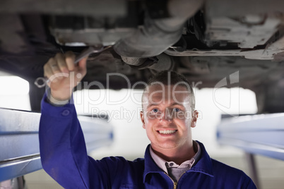Smiling mechanic repairing a car with a spanner