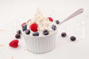 White jar of berries and whipped cream with spoon