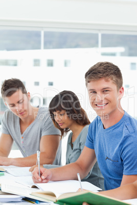 A man looks up from studying into the camera and smiles