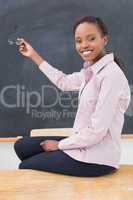 Teacher sitting on desk showing the blackboard