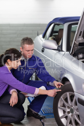 Mechanic touching the car wheel next to a woman