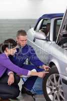 Mechanic touching the car wheel next to a woman