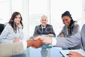 Three smiling co-workers looking at two business people shaking