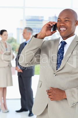 Young manager laughing on the phone while his team is in the bac
