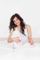 Smiling brunette woman sitting on her bed