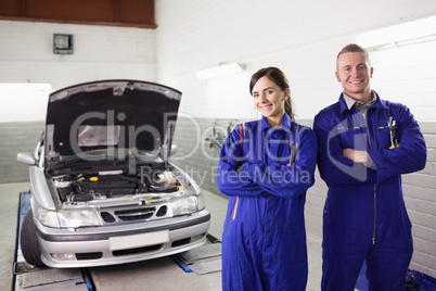 Smiling mechanics with arms crossed next to a car