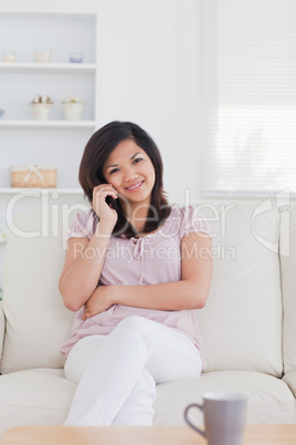 Smiling woman phoning while sitting on a couch