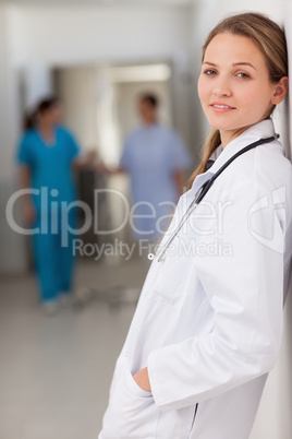 Smiling doctor standing against a wall with her hands in her poc