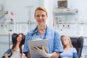 Nurse writing on a clipboard next to patients