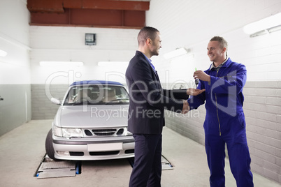 Mechanic giving car key while shaking hand to a client
